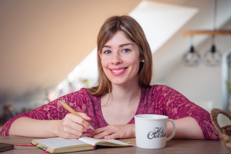 Rebecca Janko strahlt in die Kamera und schreibt gerade einige Ideen in ihr Notizbuch, um kreative Texte zu schreiben, die deine Wunschkunden ansprechen